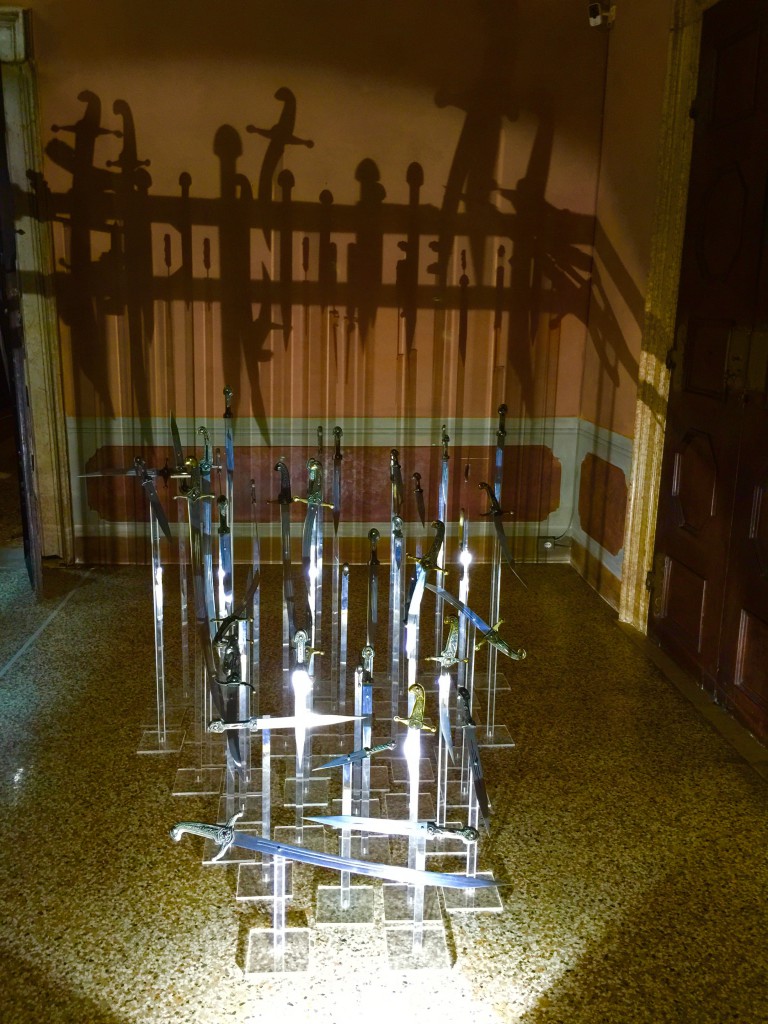 An art installation, part of the Venice Biennale at the Barbaro Palace. The position of the swords alone cast the shadow that spells out the message.